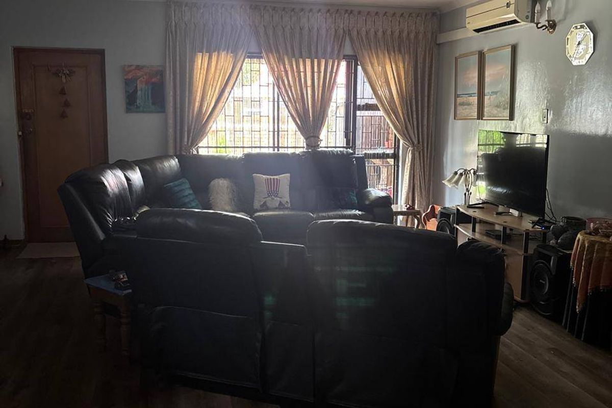 A comfortable living room featuring laminate flooring, a wall-mounted air conditioning unit, and security bars on the windows.
