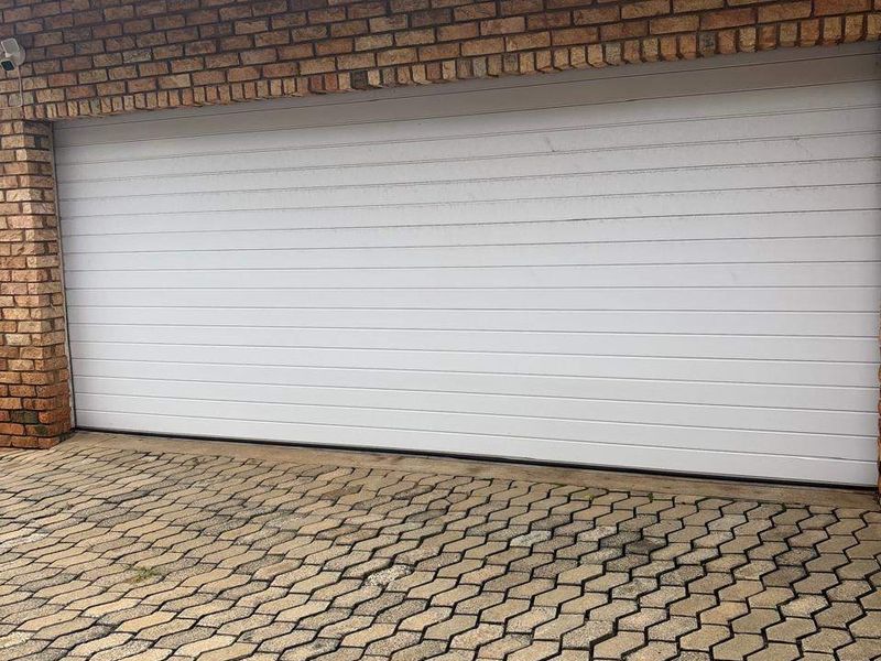 A view of a double garage featuring a white sectional door, brick exterior walls, and a paved driveway.