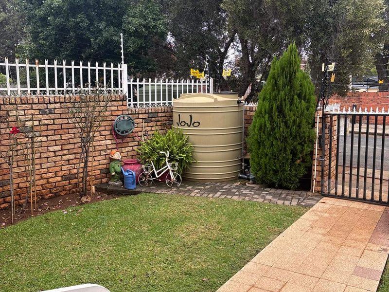 Front garden area featuring a paved walkway, lawn, brick boundary wall with electric fencing, and a water storage tank.