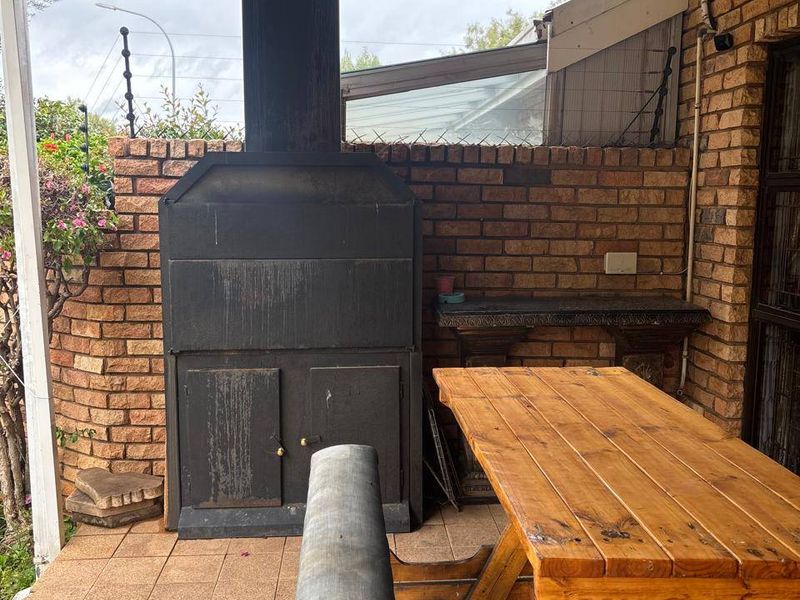Covered patio area featuring a built-in braai, brick wall finishes, and tiled flooring, providing a functional outdoor entertainment space.