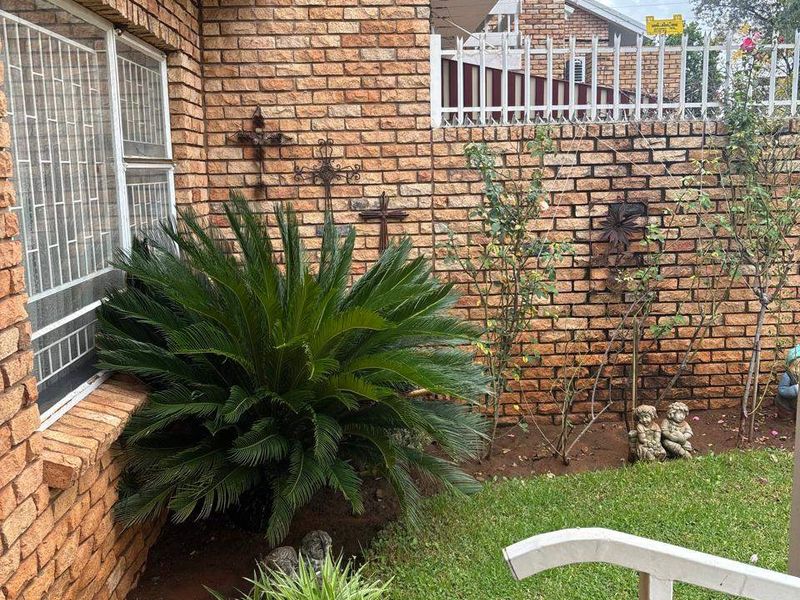 A private rear garden area featuring face brick exterior walls, security window bars, and established garden beds with lawn.