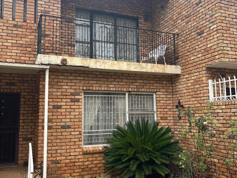 Rear view of a double-story face brick townhouse featuring a balcony with wrought iron railings, security bars, and a small private garden area.