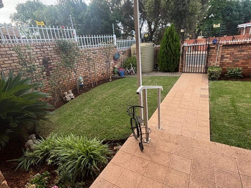 A private rear garden featuring a tiled patio, manicured lawn, brick boundary walls with electric fencing, and a water tank.