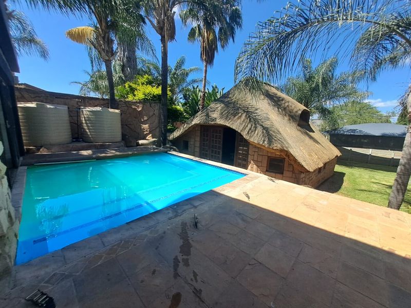 Outdoor pool area featuring a paved patio, swimming pool, and a traditional thatch roof lapa structure with stone wall finishes.