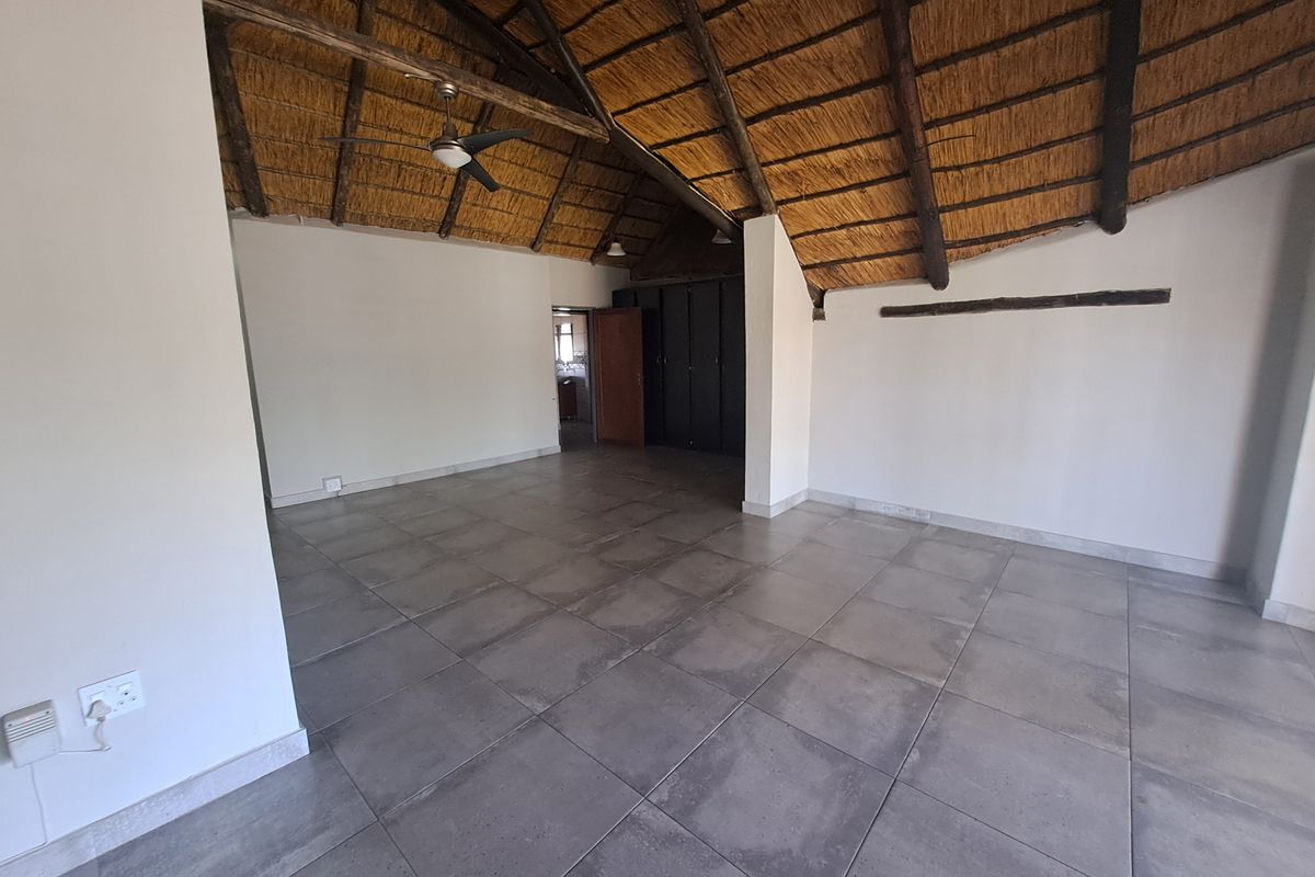 Spacious living area featuring a high thatched roof with exposed timber rafters, tiled flooring, and built-in storage cupboards.