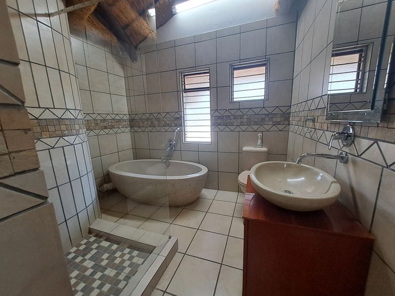 A bathroom featuring a freestanding bathtub, vessel sink, walk-in shower, and tiled finishes under a vaulted thatch roof.