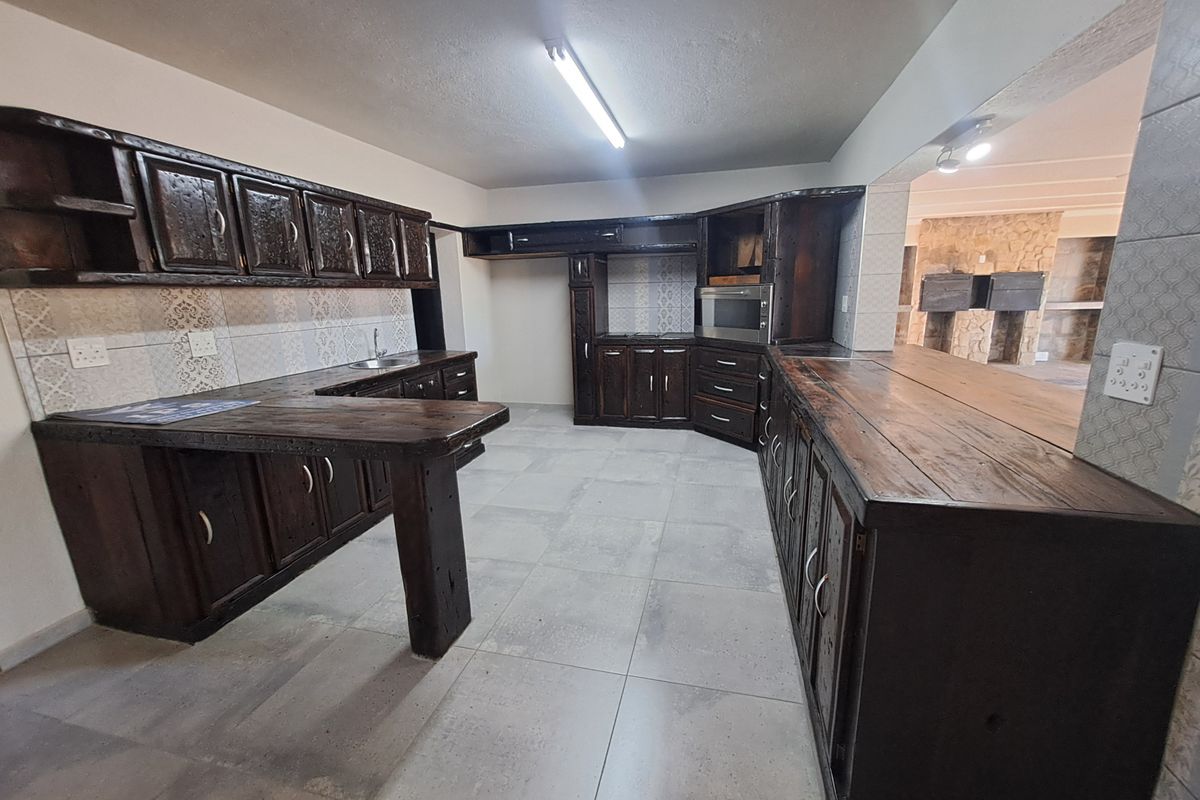 Spacious kitchen featuring dark wood cabinetry, tiled backsplash, built-in oven, and a functional breakfast bar area with neutral floor tiles.