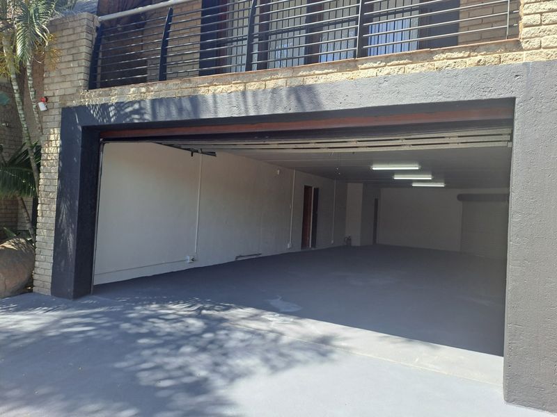 Spacious double garage with painted concrete flooring, fluorescent lighting, and direct access to the property, featuring a brick exterior and upper balcony.