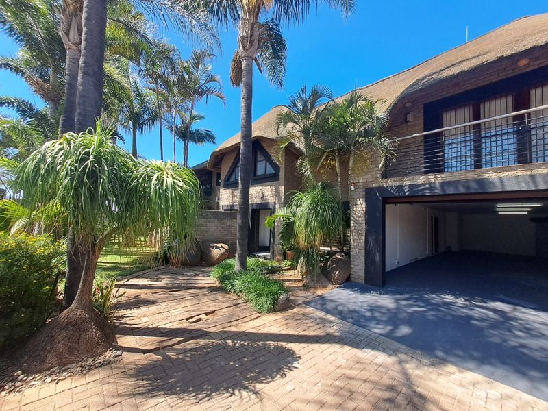 Front exterior view of a double-story house featuring a traditional thatch roof, brick facade, paved driveway, and an integrated double garage.