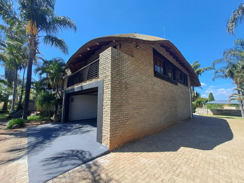 Exterior view of a face brick building featuring a thatched roof, a garage, and an upper-level balcony, set on a paved driveway.