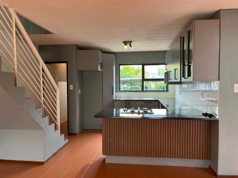 Open-plan kitchen featuring modern cabinetry, a gas hob, and tiled flooring, seamlessly integrated with a staircase leading to the upper level.