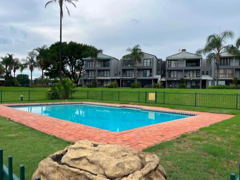 A well-maintained communal swimming pool area featuring brick coping and metal fencing, set against a backdrop of multi-story townhouse units and landscaped grounds.