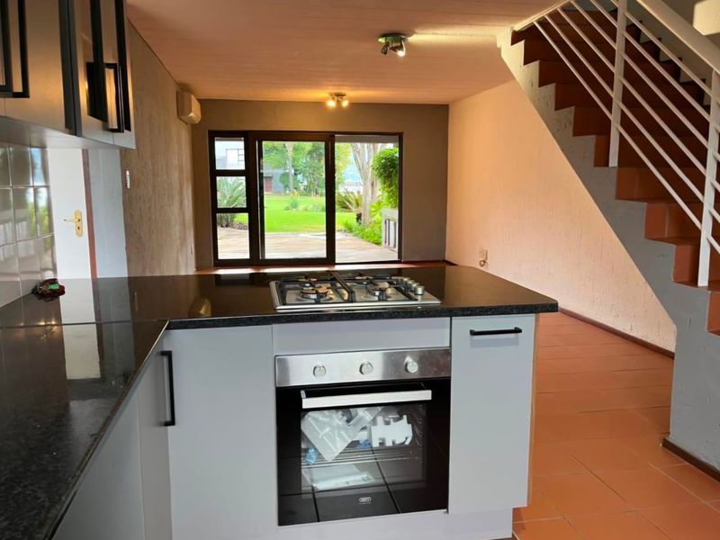 Open-plan kitchen and living area featuring a modern built-in oven, gas hob, granite countertops, and direct access to the garden through sliding glass doors.