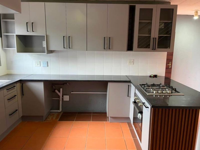 A functional kitchen featuring grey cabinetry, granite countertops, a gas hob, and a built-in oven, with tiled flooring and backsplash.