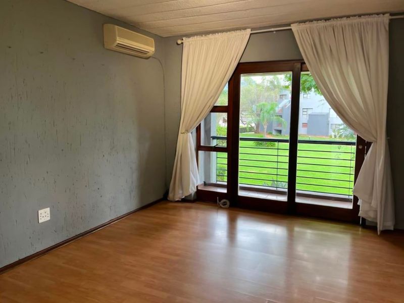 An empty living room featuring laminate flooring, a wall-mounted air conditioning unit, and sliding glass doors leading to a balcony.