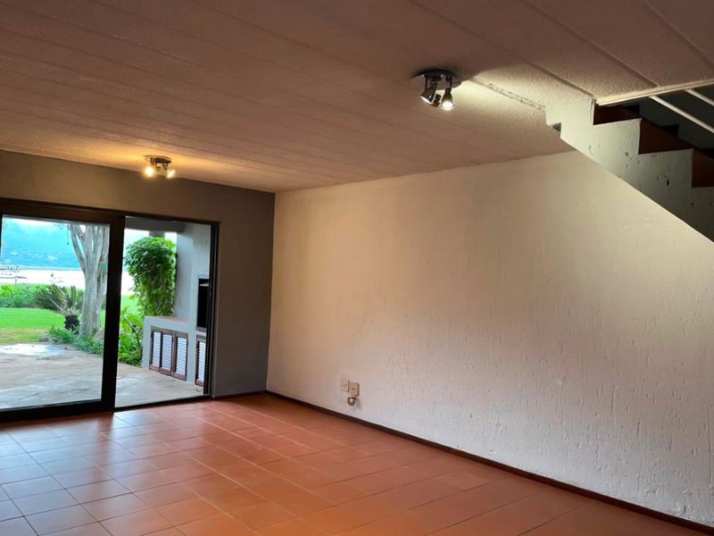 Spacious open-plan living area featuring terracotta floor tiles, direct access to the patio through sliding glass doors, and an integrated staircase.