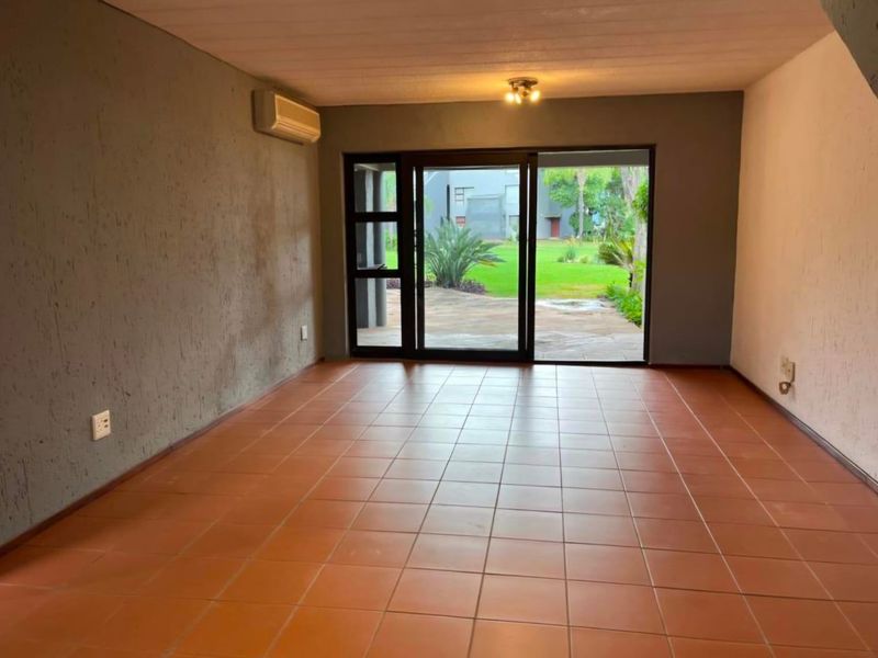 An empty living room featuring terracotta floor tiles, a wall-mounted air conditioner, and large sliding glass doors providing access to the rear garden.