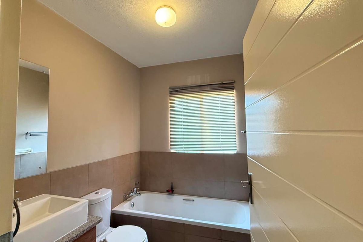 A functional bathroom featuring a bathtub, toilet, and vanity basin with neutral wall tones and tiled splashbacks.