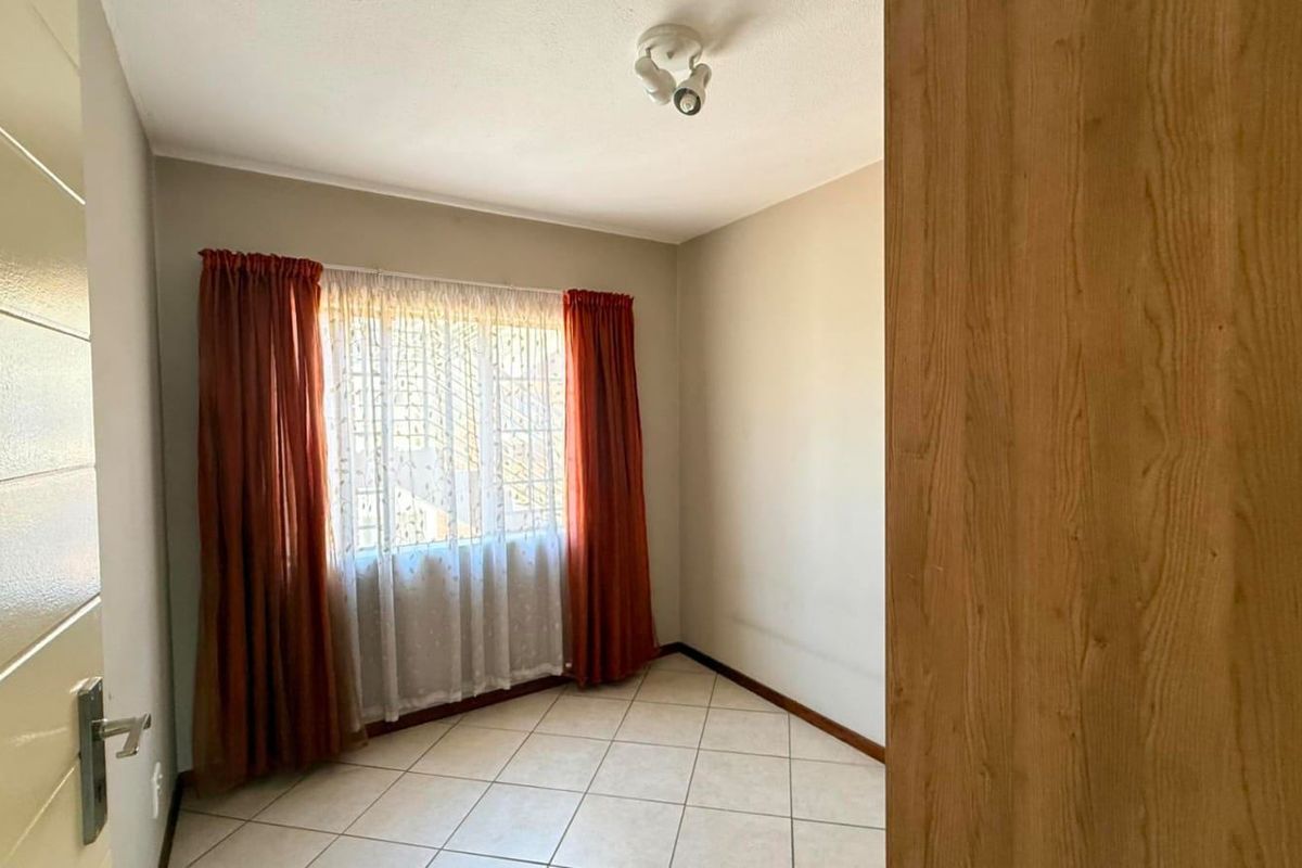 A clean, empty bedroom featuring neutral tiled flooring and a built-in wooden cupboard, offering a blank canvas for personalization.