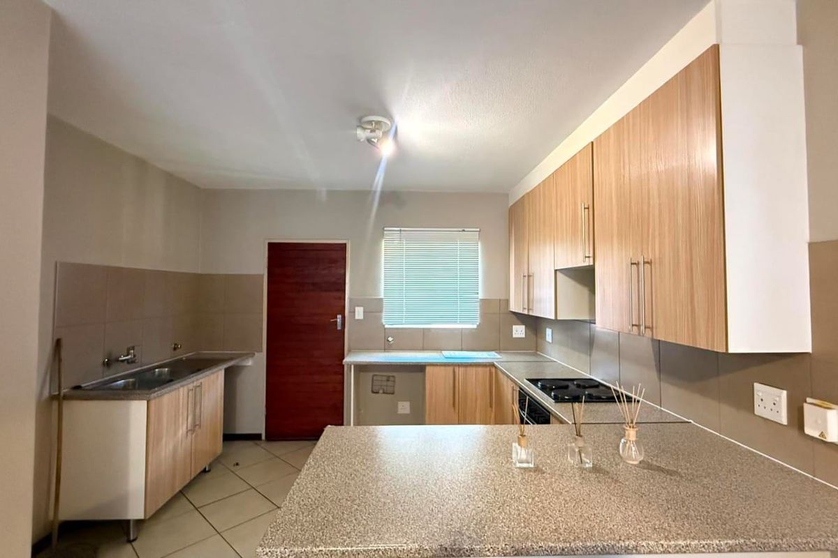 A functional kitchen featuring light wood-finish cabinetry, granite-look countertops, a built-in hob, and tiled flooring, offering a clean and practical workspace.