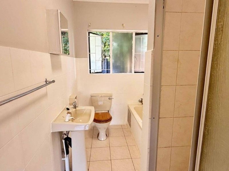 A functional bathroom featuring a pedestal basin, toilet, and built-in bathtub with tiled finishes, offering potential for modernization and cosmetic updates.
