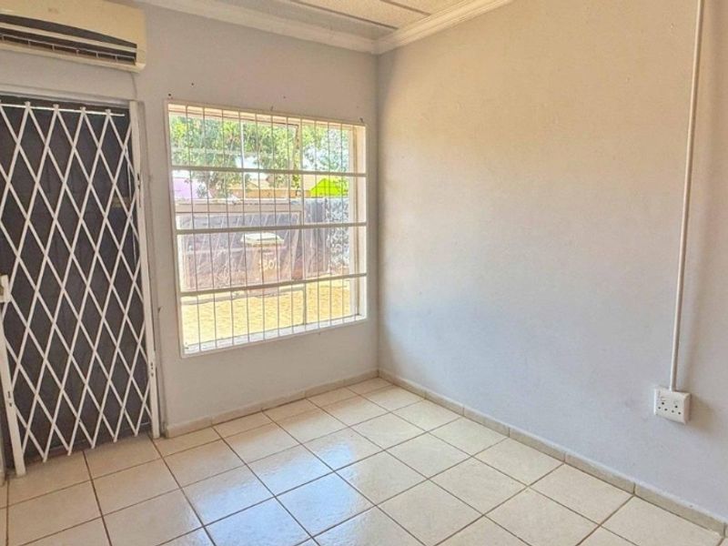 An empty living area featuring tiled flooring, a wall-mounted air conditioning unit, and security bars on the window and door.