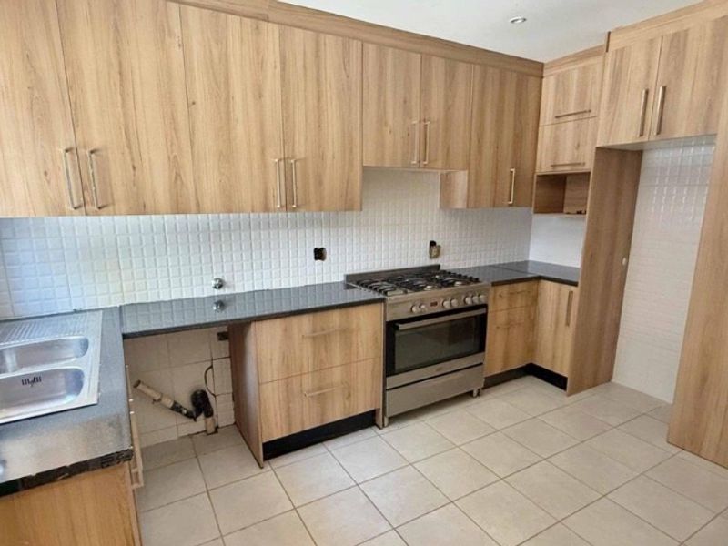 A functional kitchen featuring light wood cabinetry, granite countertops, a gas stove, and a tiled backsplash, currently vacant and ready for customization.