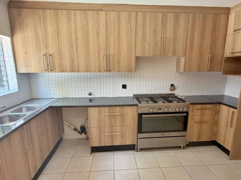 A functional kitchen featuring wood-look cabinetry, dark granite countertops, a stainless steel gas stove, and a double sink with tiled backsplash.