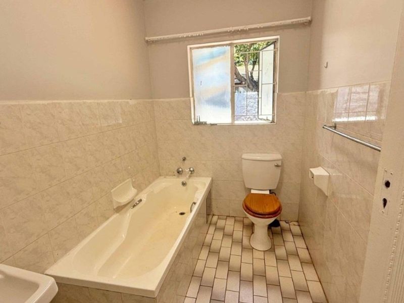 A dated bathroom featuring a standard bathtub, toilet, and tiled finishes, requiring cosmetic updates to modernize the space.