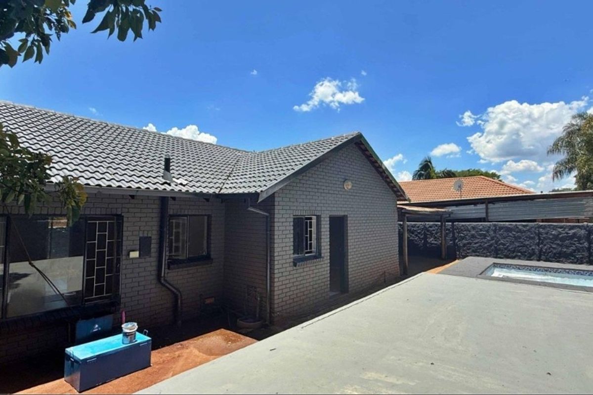 Rear view of the property featuring a brick facade, tiled roof, and a swimming pool area with a concrete patio.