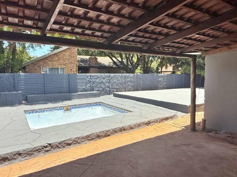 Outdoor pool area featuring a covered patio with timber pergola, concrete paving, and a swimming pool, currently undergoing renovation.