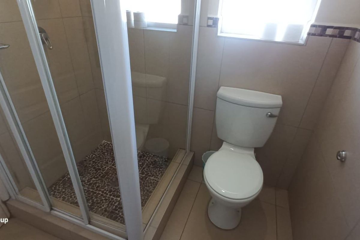 A functional bathroom featuring a glass-enclosed shower cubicle and a standard white toilet with neutral wall and floor tiling.