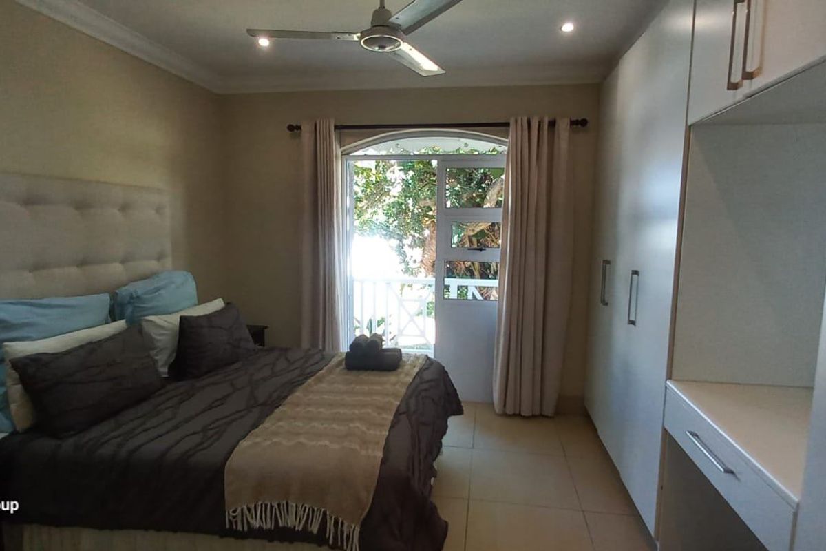 A well-maintained bedroom featuring built-in cupboards, a ceiling fan, and a glass door providing access to an outdoor balcony area.