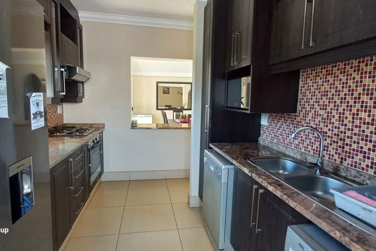 A functional kitchen featuring dark cabinetry, granite countertops, a mosaic tile backsplash, and a convenient serving hatch opening into the adjacent living area.