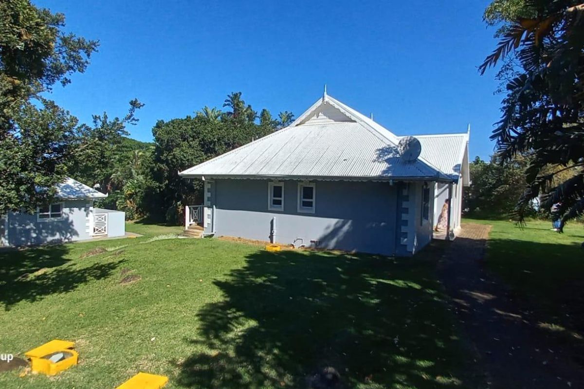 A view of the rear exterior of the house, featuring a metal roof, grey painted walls, and a spacious surrounding garden area.