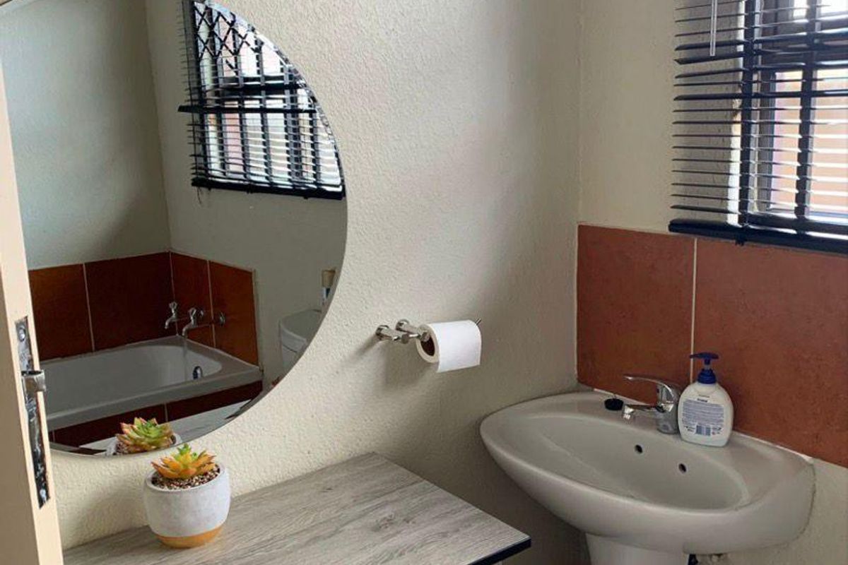 A functional bathroom featuring a pedestal basin, built-in vanity cabinet, round mirror, and a bathtub with tiled splashback.