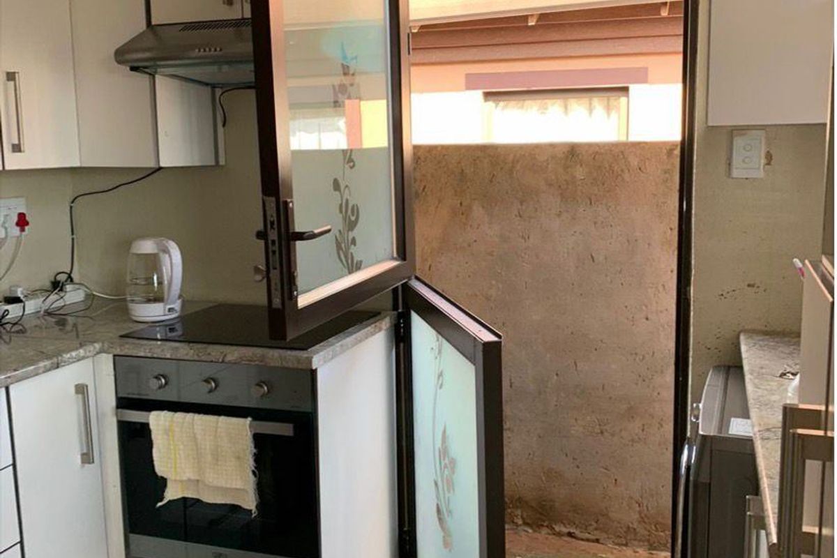 Compact kitchen featuring white cabinetry, stone-look countertops, built-in oven and hob, and a stable door providing direct access to the exterior.