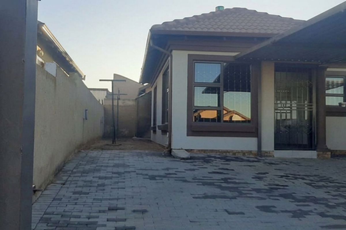 Front view of a residential house featuring a paved driveway, covered carport, and secure boundary walling.