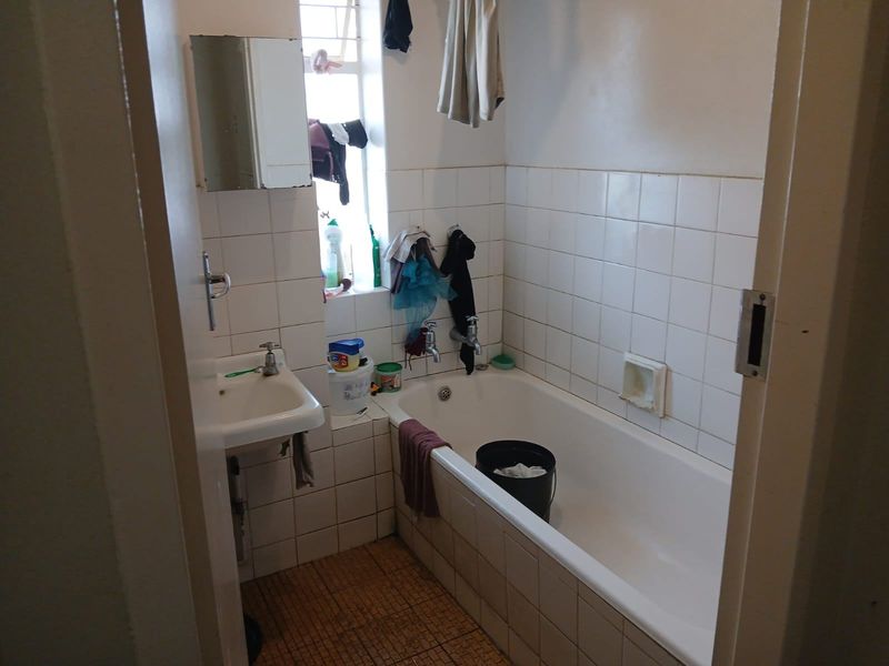 A compact bathroom featuring a standard bathtub, wall-mounted basin, and tiled finishes, offering a functional space in need of cosmetic updates.