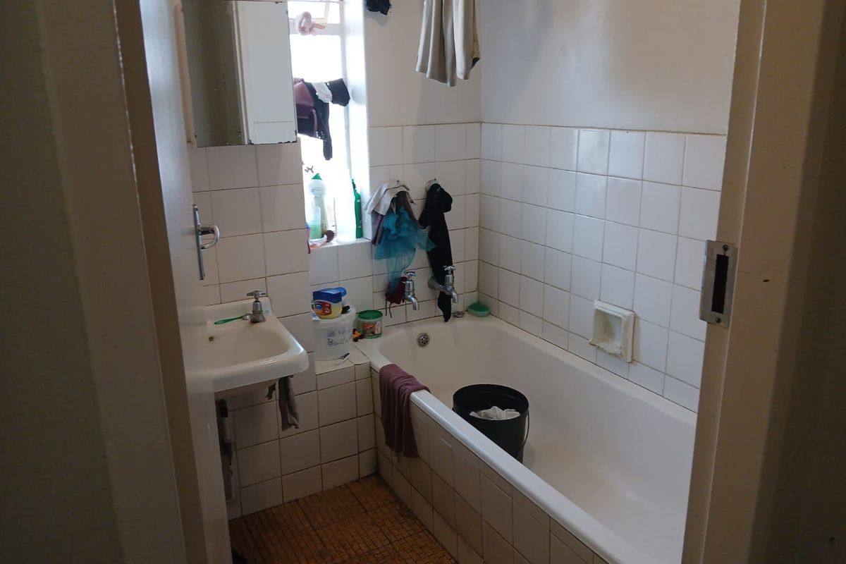 A compact bathroom featuring a standard bathtub, wall-mounted basin, and tiled finishes, offering a functional space in need of cosmetic updates.