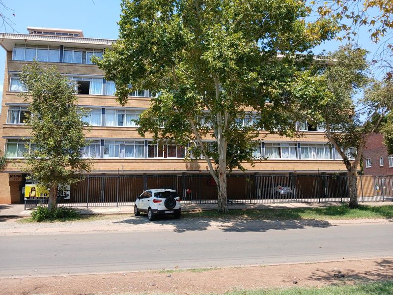 Front elevation of a multi-story brick apartment building featuring large windows and secure ground-level parking behind metal fencing.