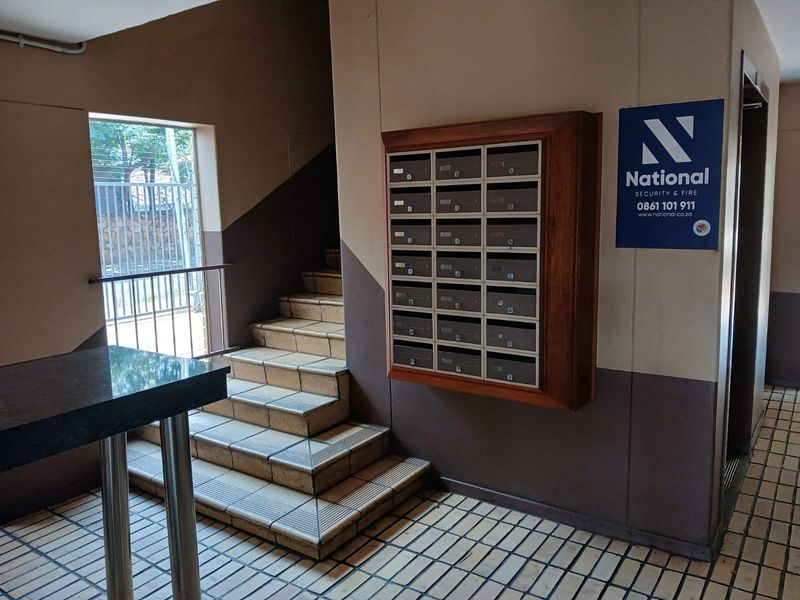 Apartment building entrance lobby featuring a tiled staircase, a wall-mounted bank of mailboxes, and security signage.