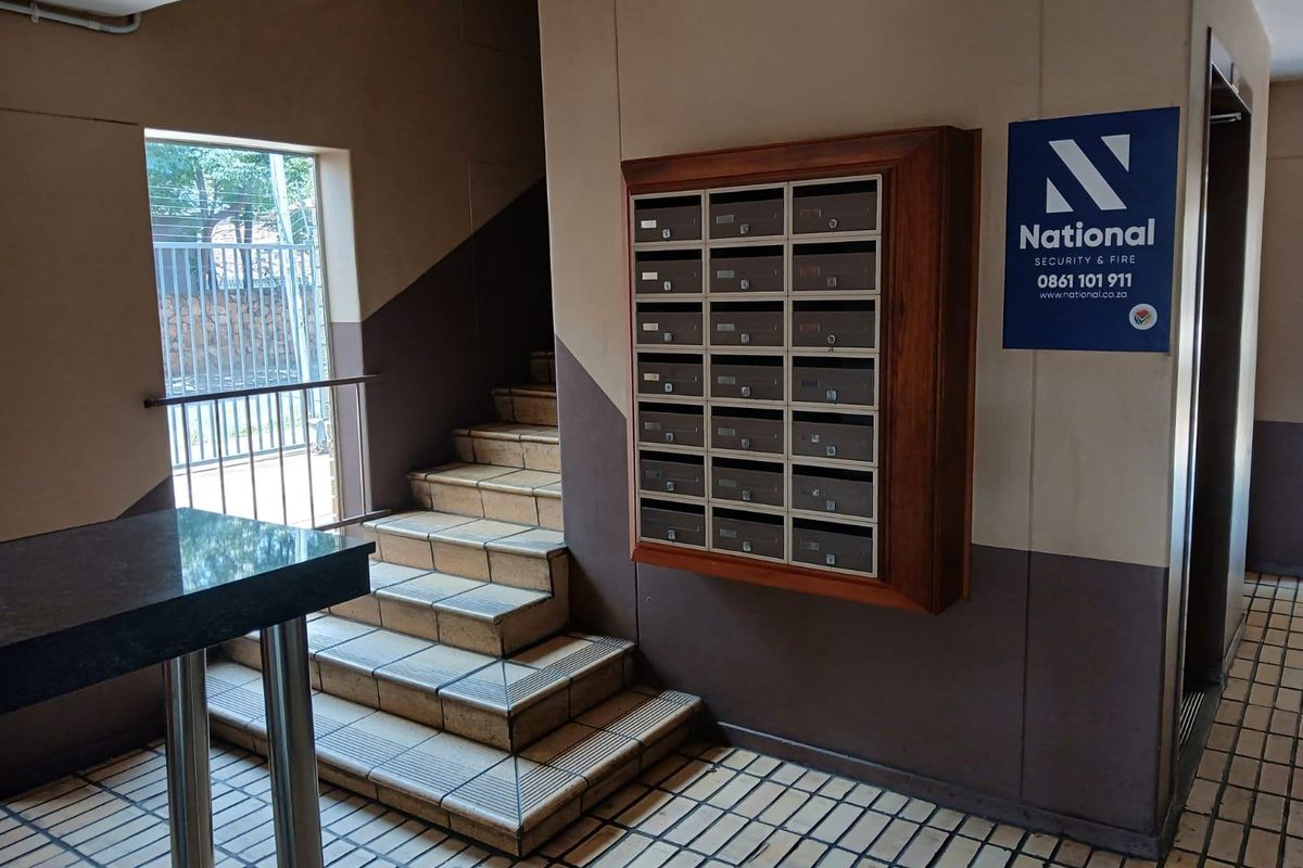 Apartment building entrance lobby featuring a tiled staircase, a wall-mounted bank of mailboxes, and security signage.