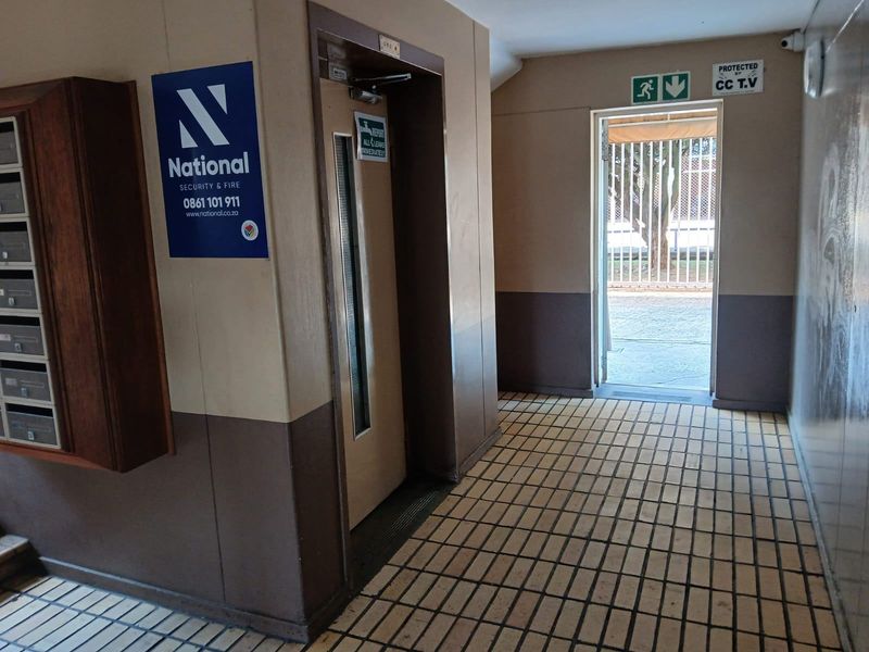 Apartment building entrance lobby featuring tiled flooring, a functional elevator, wall-mounted mailboxes, and security surveillance.