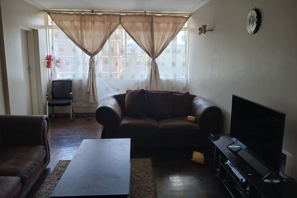 A living room featuring large windows that provide natural light and dark hardwood flooring throughout the space.