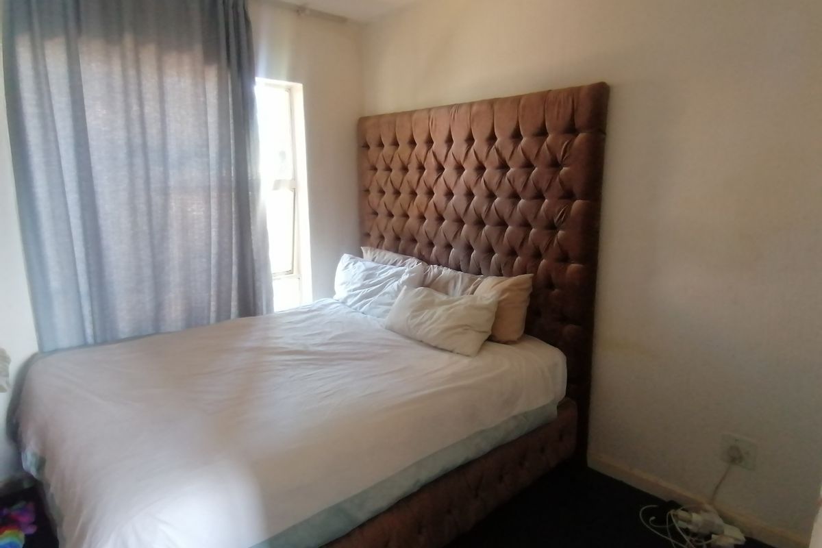 A bedroom featuring a window with curtains and visible wall wear, requiring minor cosmetic updates to improve the overall finish.