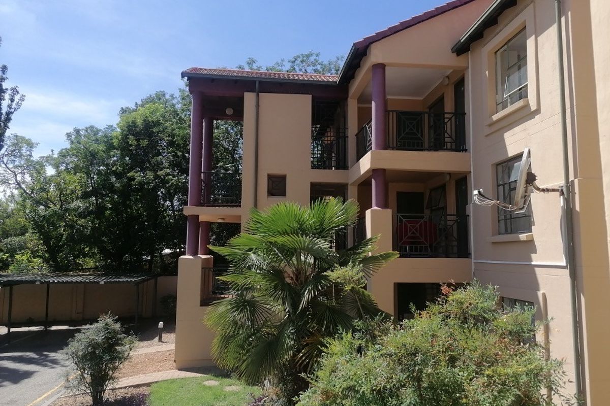 Exterior view of the apartment building featuring multi-level balconies with wrought iron railings, tiled roofing, and an adjacent covered carport area.