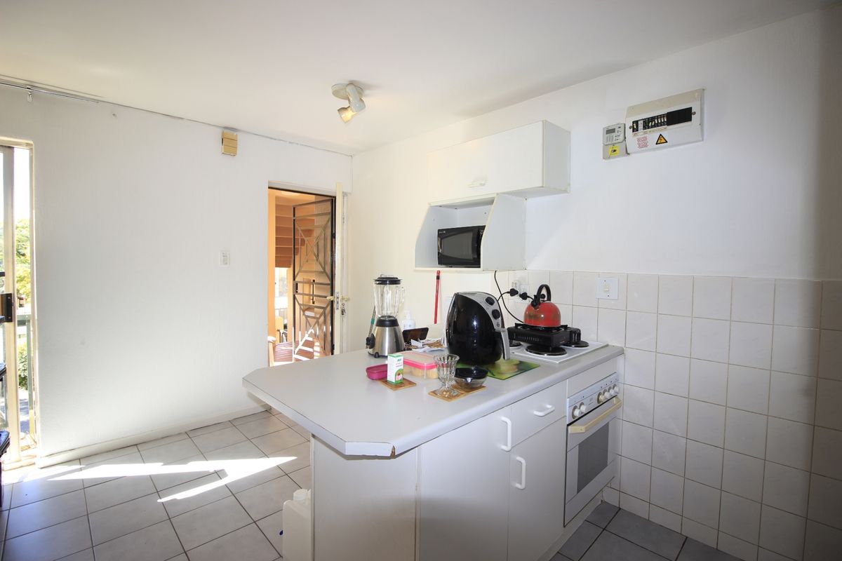 Compact kitchen featuring built-in oven, hob, tiled splashback, and white cabinetry, with direct access to an outdoor area.