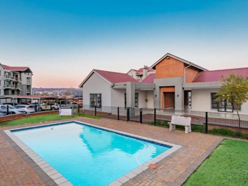 A well-maintained communal swimming pool area featuring brick paving, metal fencing, and a view of the apartment complex buildings.