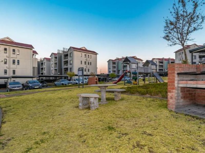 Communal garden area featuring a brick braai facility and playground equipment, set within a well-maintained apartment complex.
